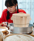 Premium Wooden Steaming Rice Basket Cooks Up Fluffy Fragrant Rice Fast in a kitchen with a young woman preparing food.