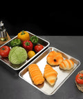 Heavy Duty Commercial 13 X 18 Half Size Aluminum Sheet Pan And Bun Tray With Sturdy Tapered Sides, showcasing colorful vegetables and baked goods.