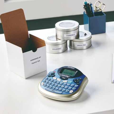 Portable Handheld Label Maker With QWERTY Keyboard And 2 Line Printing on a desk with labeled tea tins and office supplies.