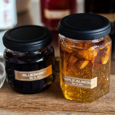 Two jars with labels: one with blueberry spread, one with maple almond spread, showing labeled jars on a wooden surface.