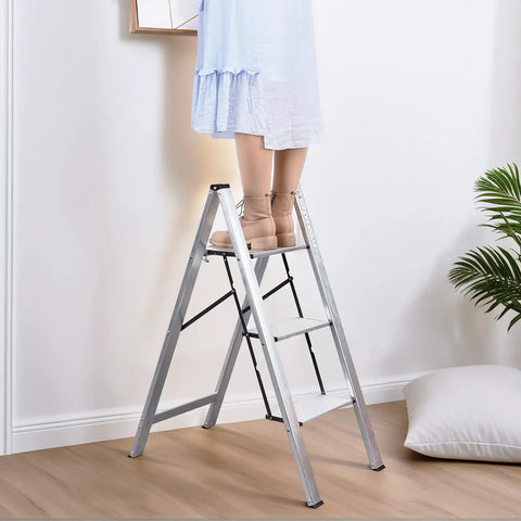 Person standing on a Three Step Aluminum Folding Ladder For Indoor And Outdoor Tasks Space Saving Slim Fold To Four Centimeter Flat.