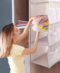 User placing folded clothes in Four Tier Hanging Closet Storage Bag With Thick Oxford Fabric Drop Dead Durable Foldable Door Organizer Heavy Duty Wardrobe Rack Big Time Space Saver For Any Room.