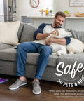Man sitting on a couch with a dog, Click N Clean Multi Surface Spray Mop visible on the floor near him.