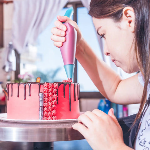 Next Level Cake Decorating Kit Featuring Hella Durable Anti Burst Piping Bags used to pipe icing on a pink cake.