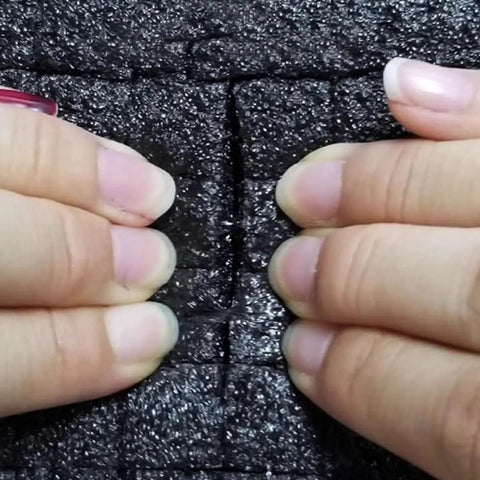 Hands pressing down on Black PE Foam Packing Sheets With Perforated Grid Design, showcasing thickness and cushioning.