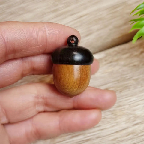 Hella Slick Screw Open Miniature Black Ebony Acorn Curios Set Of Two With Hidden Antique Bronze Pinecones For Super Dope Fall Harvest Woodland Decor, held in hand.