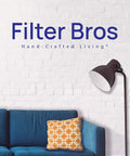 Modern living room with blue sofa, decorative cushion, floor lamp, brick wall, and text 'Filter Bros Hand-Crafted Living'