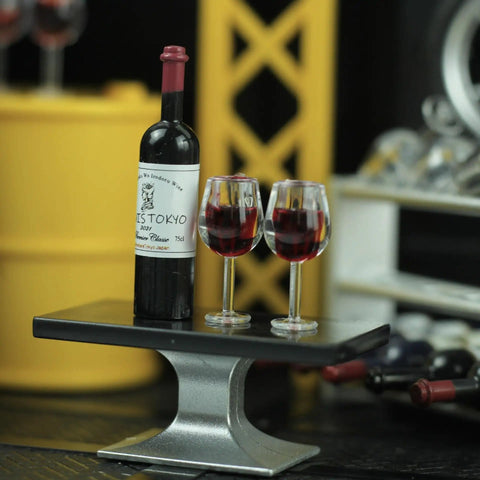 Hella Cool Miniature Red Wine Bottle Set Featuring Two Resin Filled Wine Glasses And A Static Corkscrew For Dollhouse Decor, showcasing bottle and glasses on a table.