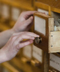 Person opening a wooden drawer with a Top Tier Mini Drawer Knob featuring durable antique finish.