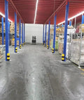 Warehouse interior with blue columns, yellow-black striped bumpers, showcasing Built Tough Bully Proof Heavy Duty Pallet Rack Protectors Forklift Bumper Guards For Warehouse Columns Shock Absorbing Upright Shields Yellow Black Striped Industrial Corner Covers 18 Pack.
