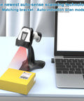 2D Handheld Wireless Barcode Scanner With Stand 3 In 1 Bluetooth Barcode And QR Scanner on a desk beside a laptop and package