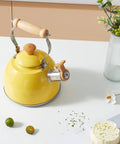 Yellow 1.6 Quart Tea Kettle With Cool Touch Wooden Handle Food Grade Stainless Steel Stovetop Teapot Whistling Kettle For Easy Pour Ergonomic Grip Safe Heat Resistant Kitchen Accessory displayed on a kitchen table.