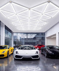 Hexagon Garage Lighting System Bundle For Full Coverage Pro Grade LED Ceiling Lights Great For Car Detailing Workshop And Commercial Use 132 Sq Ft 71 Piece Modular Kit No Shadow No Glare installed in a garage over sports cars.