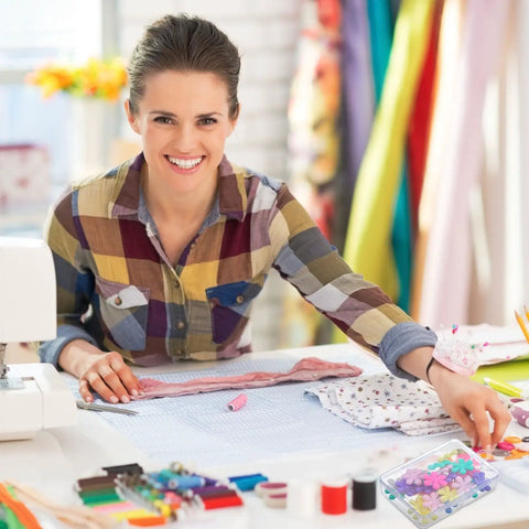 Smiling woman sewing with 30 Piece Needle Threader Set with Clear Box Multicolor Flower Head Wire Loop Threaders on a table.