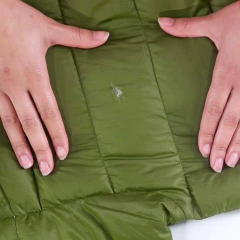 Hands repairing tear on green fabric with Tenacious Tape Mini Patches With Peel And Stick Adhesive For Holes And Tears In Winter Gear.
