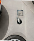 Badass 4 Inch Rubber Gate Wheel Caster Featuring An Adjustable Spring Bracket mounted on concrete surface near vehicle tire.