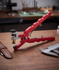 Pro Level Watch Band Tool Kit Featuring Heavy Duty Spring Bar Pliers And Precision Hole Punch For Leather Straps showing red pliers and brown leather strap on wooden table.
