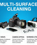 DSLR camera with lens, black binoculars, white VR headset, smartphone, and glasses on a white surface