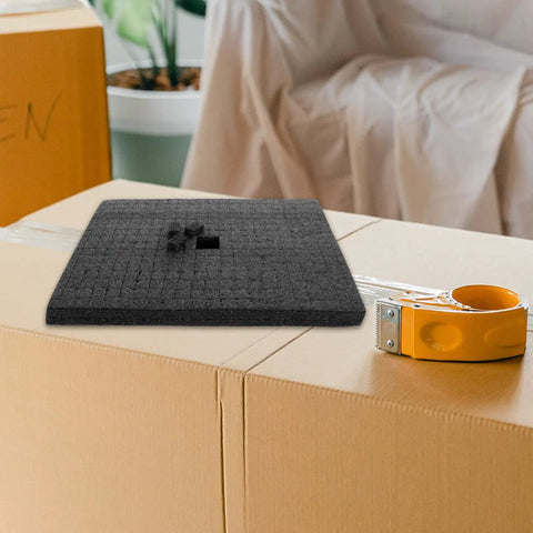 Custom Cut Black Packing Foam Insert Pad Rock Solid Cushion Block atop cardboard boxes with packing tape for shipping