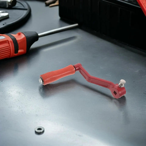 Red hand crank honey extractor handle in stainless steel for beekeeping, replacement part for bee farmers on a workbench.