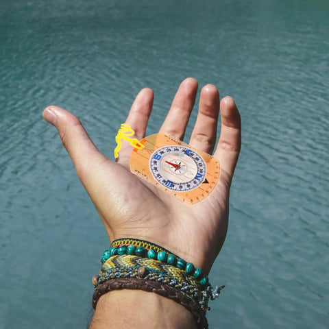 Rugged Orange Orienteering Hiking Compass With Lanyard For Hiking Camping And Backpacking held in hand near water