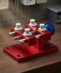 Beefy Aluminum Work Holder With Anodized Red Finish And Knurled Blue Adjustment Knob A Solid Workshop Tool For Securely Holding Parts And Precise Repairs Heavy Duty Aluminum Alloy Build For Everyday Shop Use. red aluminum work holder on bench with blue knob