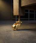 Heavy Duty Vintage Brass Swivel Caster Wheels With Cushioned Rubber Tread Set Of 4 under a wooden table leg, showcasing detailed construction.