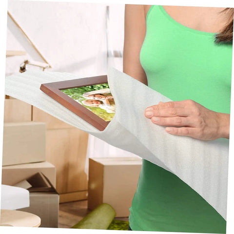 A person using 100 Pack White EPE Foam Pouches For Moving And Shipping Sweet Protective Cushioning Wrap Bags For Fragile Plates And Delicate Glassware to wrap a framed photo.