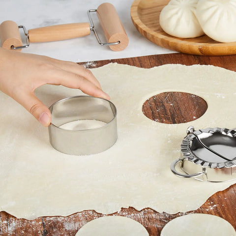 Hand using a stainless steel dough cutter on rolled dough for making dumplings for Real Deal 10 Inch Bamboo Steamer Basket Set.