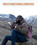 Person holding a Multi Function Hiking Compass With Luminous Scale, Mirror, And Ruler For Camping And Survival in a mountain setting.