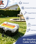 Heavy Duty Outdoor Electrical Box With IP54 Weatherproof Shield And Dual Cable Ports For Power Strips Plugs And Holiday Lights Black One Pack in a garden setting.