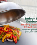 Hand lifting 12 inch stainless cheese melt dome off colorful veggies on flat griddle, showing use on indoor and outdoor grills.