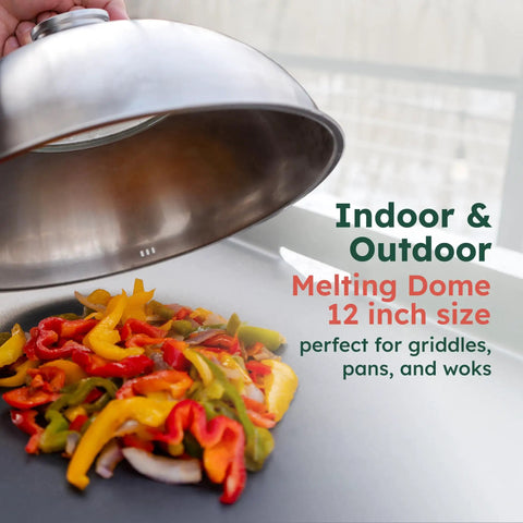 Hand lifting 12 inch stainless cheese melt dome off colorful veggies on flat griddle, showing use on indoor and outdoor grills.