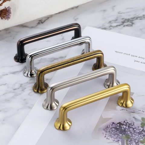 Assorted cabinet pull handles in various finishes on a marble surface, including oil rubbed bronze with clover design, front view.