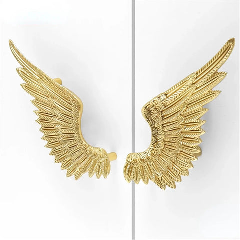 Heavy Duty Solid Brass Wardrobe Handles Featuring Slick Matte Gold Angel Wing Design And Badass Cabinet Knobs on a white cabinet door.