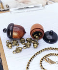 Hella Slick Screw Open Miniature Black Ebony Acorn Curios Set Of Two With Hidden Antique Bronze Pinecones showing acorns and pinecones on paper.
