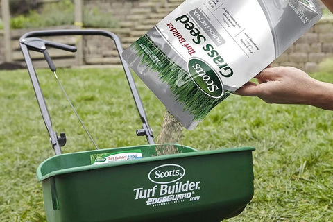Pouring Quick Kickstart Yard Patch Grass Seed Mix for fast bare spot repair into a spreader on grassy area.
