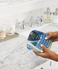Person using Portable Handheld Label Maker With QWERTY Keyboard And 2 Line Printing near a bathroom sink