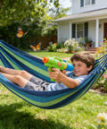 Boy relaxing in striped blue canvas hammock with water gun in yard, Canvas Hammock With Durable Comfort For Patio Yard Garden Backyard And Travel Portable And Easy Setup With Carrying Bag Included Ideal For Camping Outdoor Relaxation In Spacious 230 Centimeter Long Design For Supremely Comfortable Kick Back Anywhere