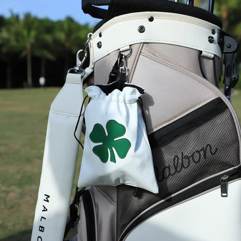 Leather Golf Valuables Pouch With Drawstrings attached to a white golf bag, featuring a green shamrock design, under sunny skies.