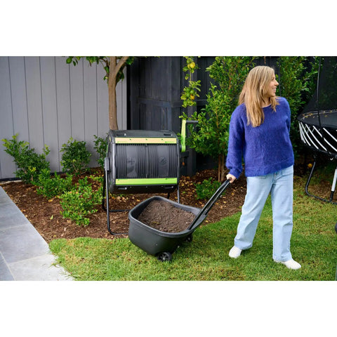 Woman using Dual Chamber 48 Gallon Compost Tumbler With Geared Rotation And Cart Access For Easy Turning Of Kitchen Scraps And Yard Waste