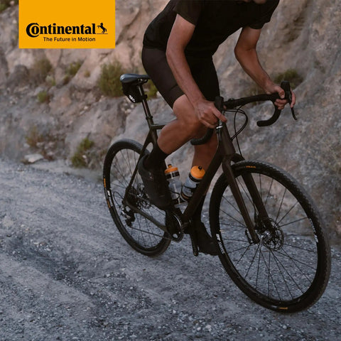 Cyclist riding a gravel bike on rugged terrain, emphasizing the use of Cross 28 Inch Inner Tubes 700x32-47c With 42mm Presta Valve Pack Of 2.