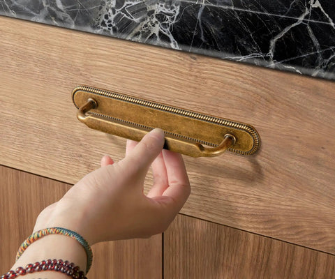 Game Changing Antique Brass Cabinet Pulls and Drawer Handles, 5 Inch Hole Center Zinc Alloy Kitchen Hardware With Vintage Backplate and Spacer, Rock Solid Corrosion Resistant Shine Makes Assembly As Easy As Pie in This 2 Pack to Spice Up Your Kitchen, hand gripping brass handle on wooden drawer.