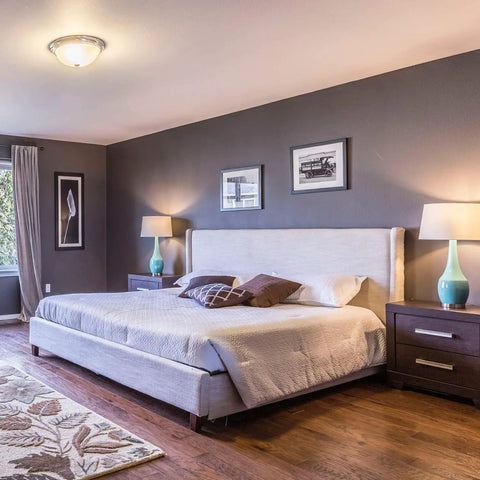Bedroom with modern décor, featuring a large bed, two side tables with lamps, and framed art on blue-gray walls.