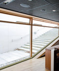 Indoor space with large glass windows and wooden interior, showing outdoor steps and natural light.