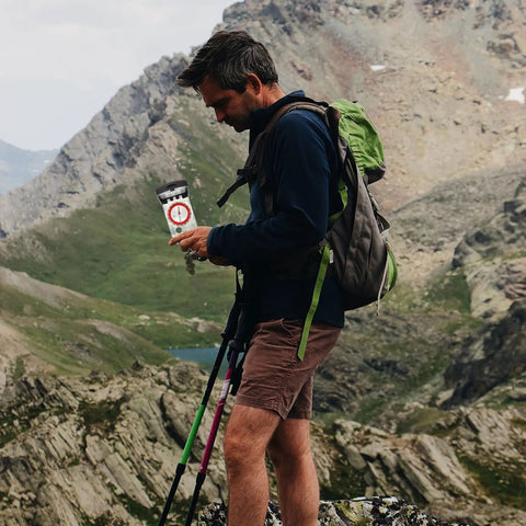Hiker using Multifunctional Outdoor Hiking Compass With Scale And Luminous Mirror For Camping while trekking in mountains.
