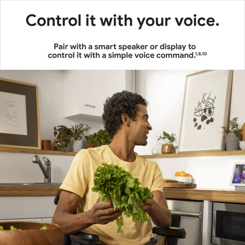 Person in kitchen holding lettuce with Indoor Nest Security Camera 1080p Wired 2nd Generation Snow Color shown on counter.