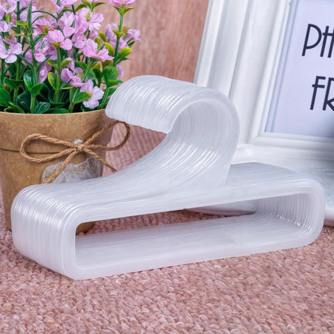 Set Of 50 White Plastic Hangers For Retail Display And Home Closet Organization, stacked on a table with decor