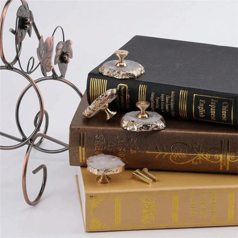 White Geode Cabinet Knobs 4 Pack Gold Plated Gemstone Drawer Pulls displayed on stacked books with metal holder.