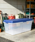 Straight Up Heavy Duty 113 Qt Long Storage Bin With Secure Snap On Lid, Crystal Clear Stackable Plastic Tote For Bulky Blankets And Seasonal Gear placed in a garage.